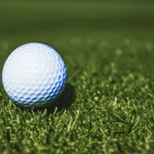 Close-up image of a white golf ball sitting on a well-manicured green grass surface