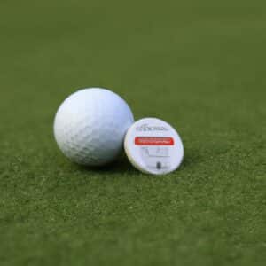 A golf ball and a golf ball marker lying on the green grass of a golf course