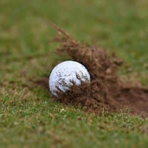 A golf ball partially buried in the soil after being hit into the ground by a golfer's swing