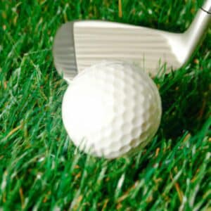 A golf ball resting on a grassy surface with a golf club poised above it