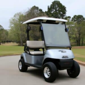 A golf cart parked on a concrete road with lush green golf course in the background