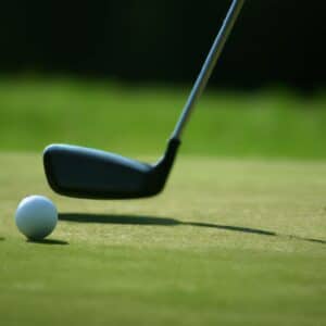 A white golf ball with the club head of a golf club positioned just behind it, ready to swing.