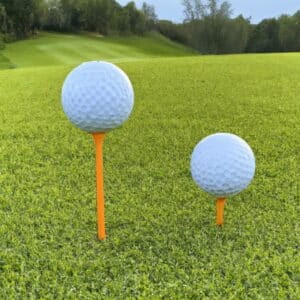 Two golf tees, one is shorter and the other is longer, with a golf ball resting on top of each.