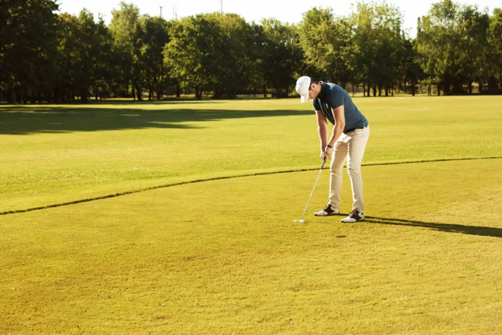 a male golfer putting golf ball in green