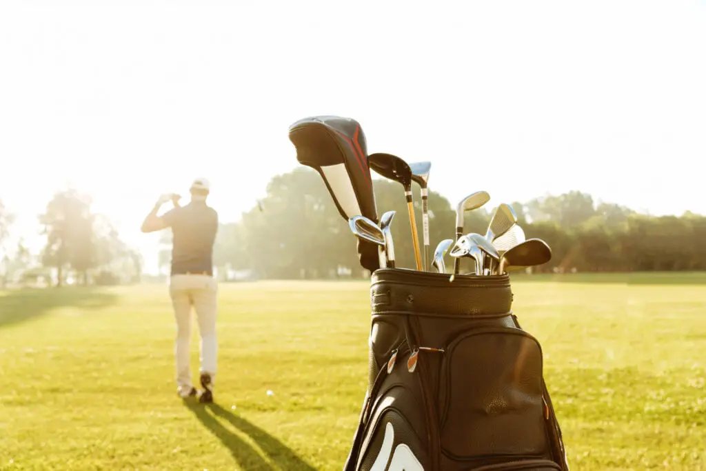 back view of male golfer swinging and his golf club bag