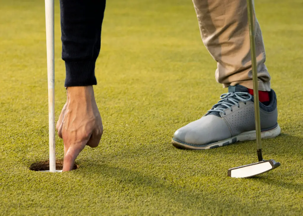 man reaching into golf ball hole with a hand